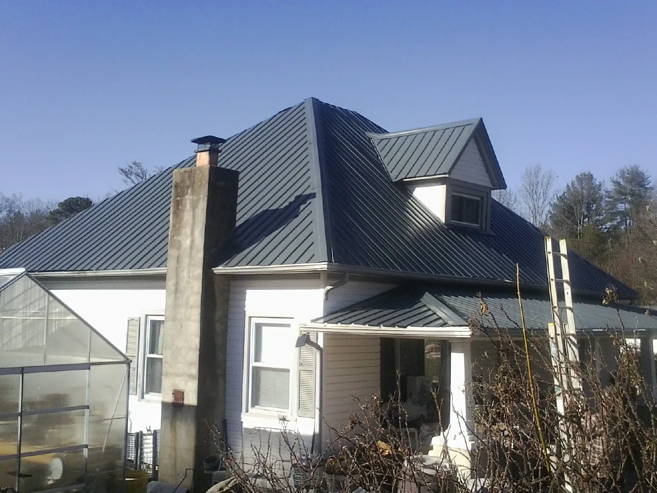 Dark blue standing seam metal roof on a white farmhouse with dormer — Slate & Tile Roof Repair by Roofing Brothers in Farnhamville