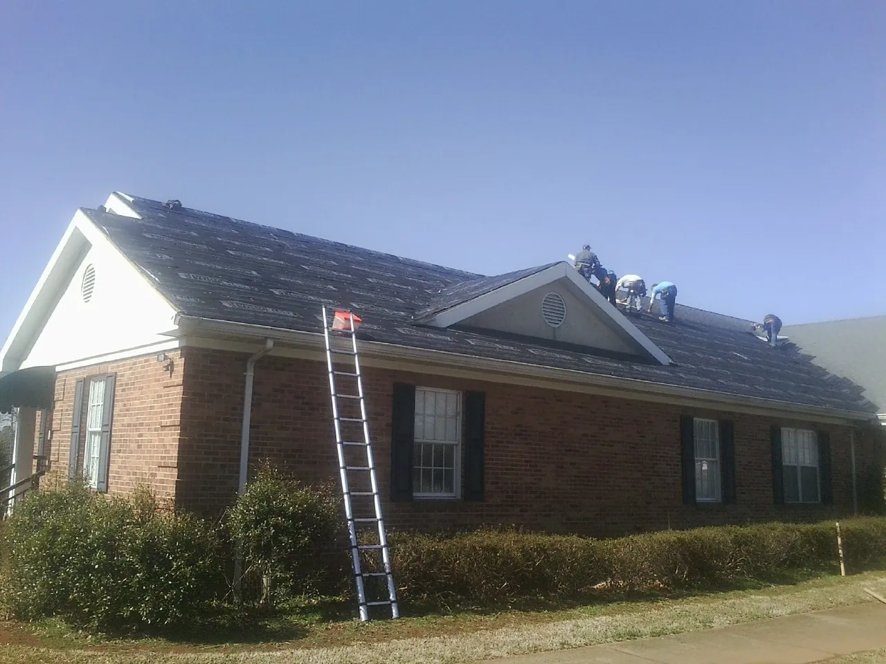Crew tearing shingles off a brick ranch roof with a ladder set — Emergency Roof Repair work by our crew in Farnhamville