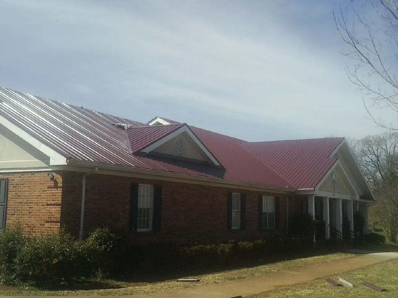 Red metal roof with gabled entries on a long brick building, from a Hail Damage Roof Repair job in Farnhamville