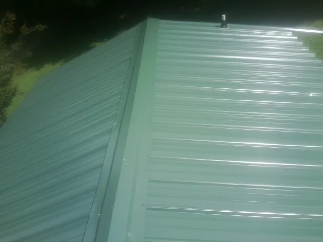 New green metal panels meeting at the ridge of a roof — Flat Roof Repair work by our crew in Farnhamville