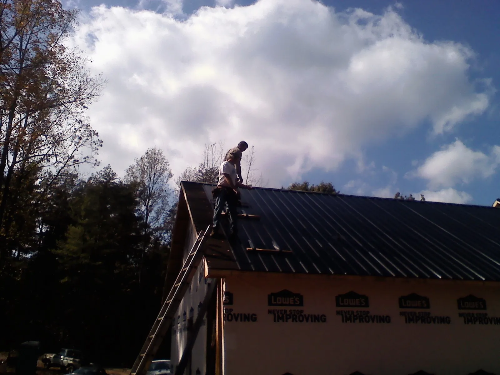 Roofer fastening dark metal panels high against a cloudy sky, from a Roof Inspection job in Farnhamville