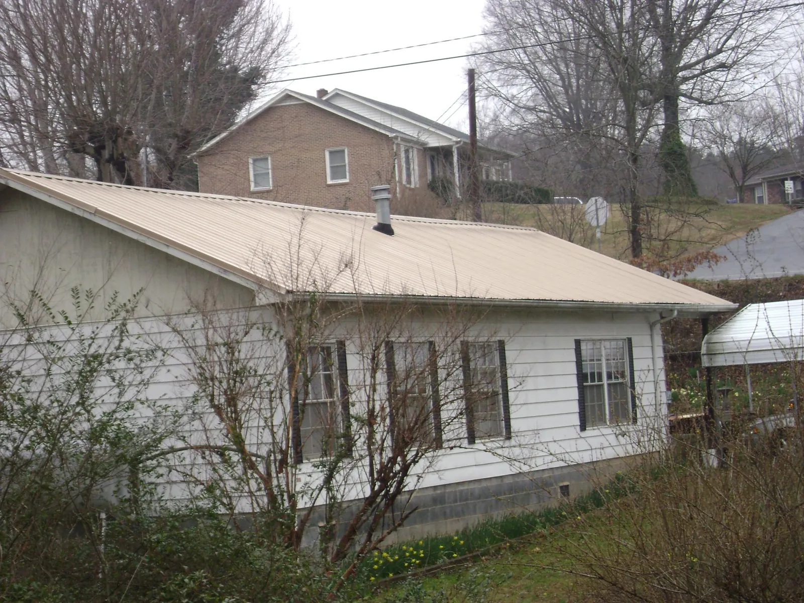 Tan metal roof on a white sided house set into a hillside — Commercial Roofing by Roofing Brothers in Farnhamville