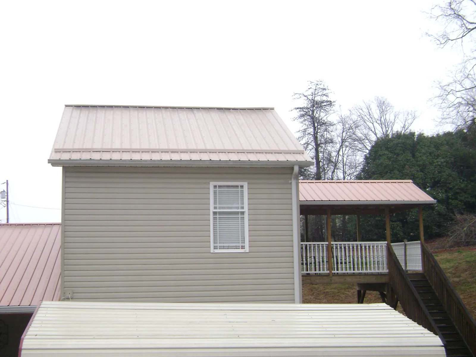 Tan metal roofs on a two story addition and attached porch, from a Roof Replacement job in Farnhamville